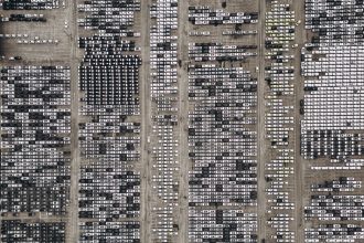 Vista aérea de um amplo estacionamento repleto de veículos novos no Brasil