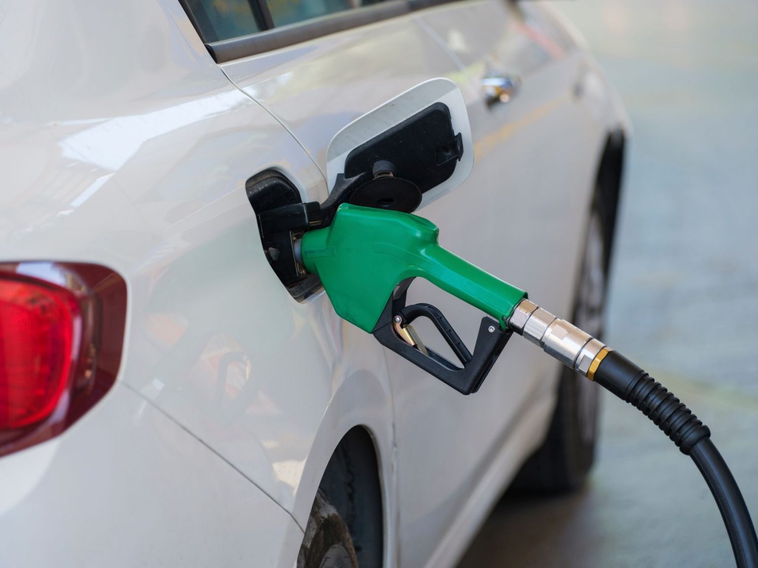 Bico verde abastece um carro branco em um posto de combustíveis.