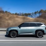 SUV elétrico trafega por uma rodovia sob céu azul e paisagem ao fundo.
