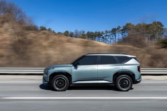SUV elétrico trafega por uma rodovia sob céu azul e paisagem ao fundo.