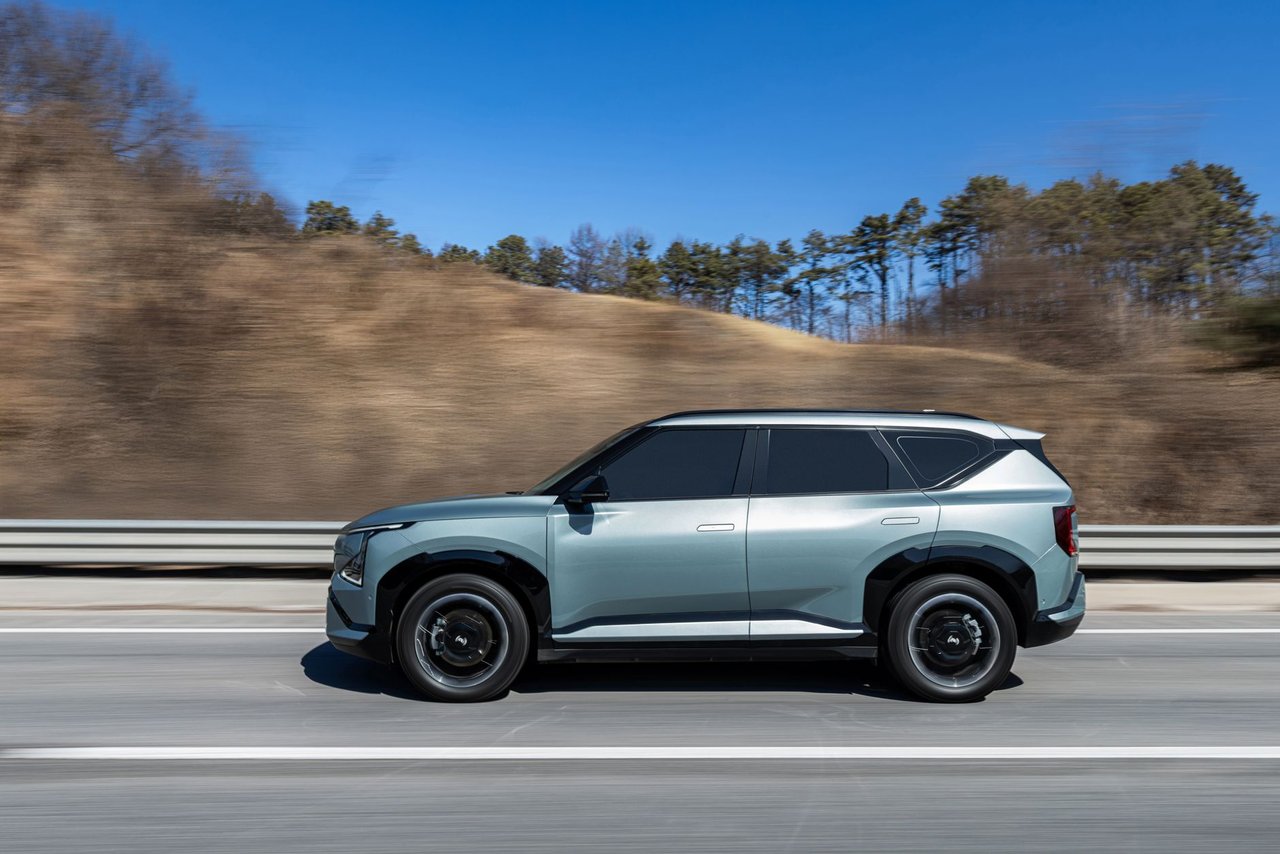 SUV elétrico trafega por uma rodovia sob céu azul e paisagem ao fundo.