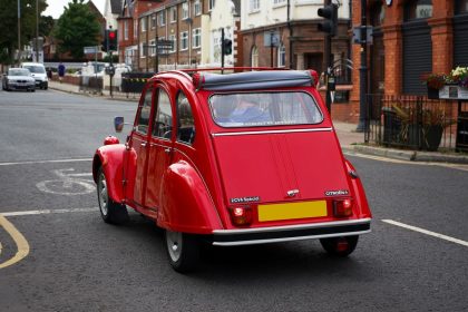 Citroën 2 CV clássico vermelho circulando por uma rua de Liverpool.