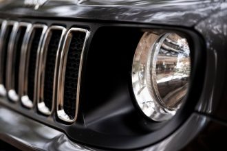Detalhe da dianteira de um SUV Jeep preto, com destaque para a grade e o farol.