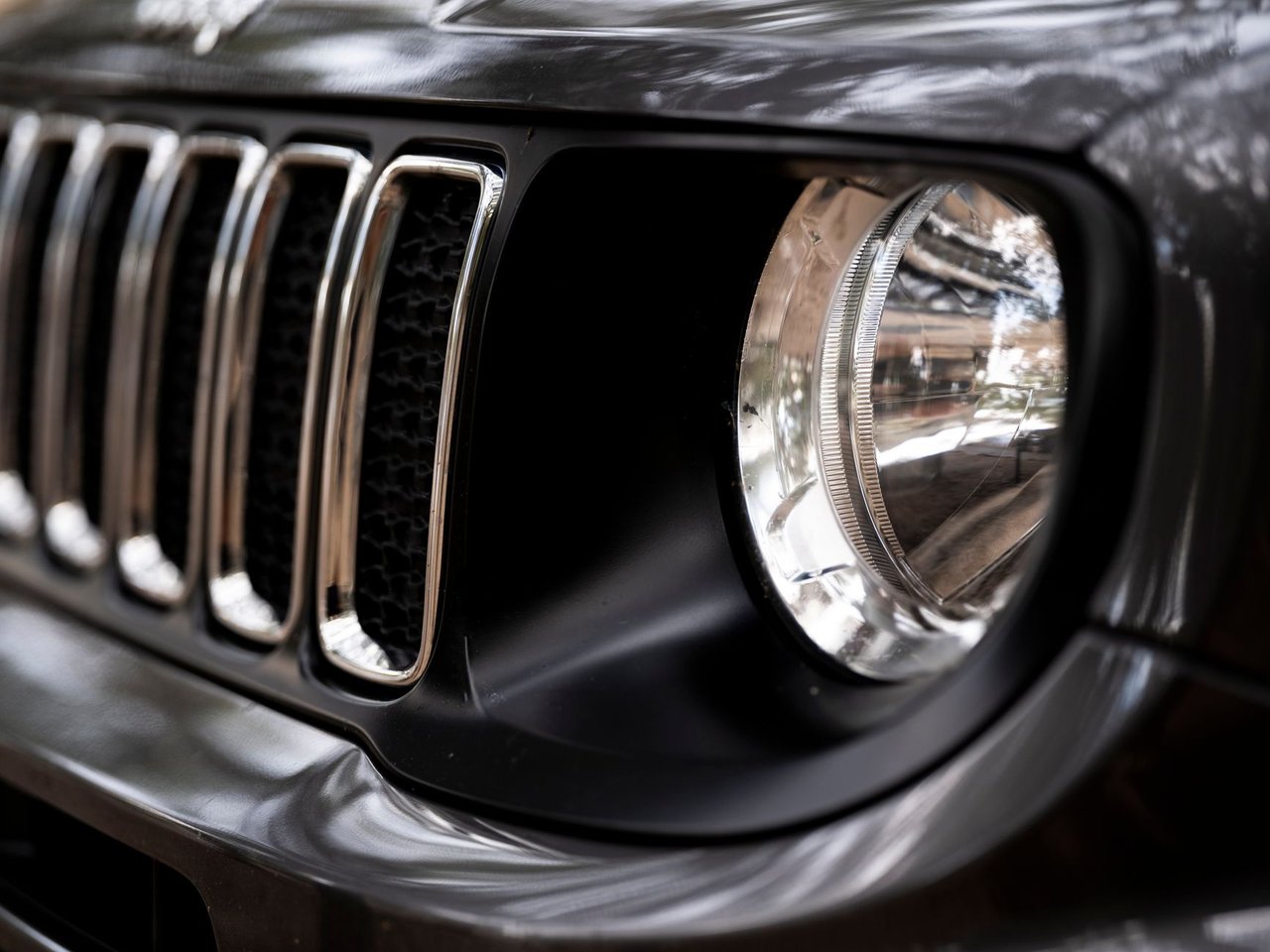 Detalhe da dianteira de um SUV Jeep preto, com destaque para a grade e o farol.