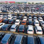 Vista aérea de fileiras de automóveis novos estacionados em uma área industrial.