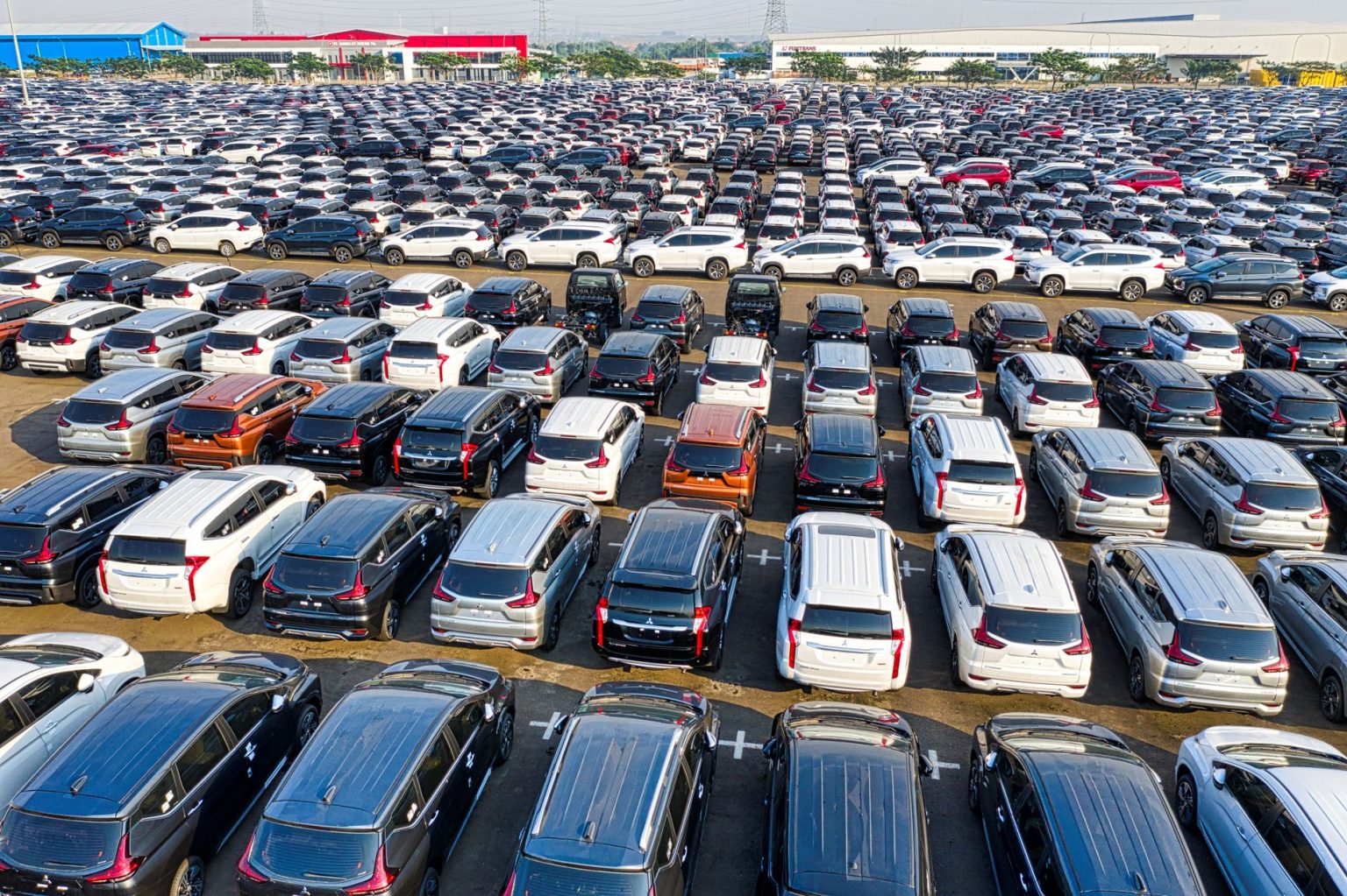 Vista aérea de fileiras de automóveis novos estacionados em uma área industrial.