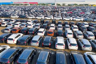 Vista aérea de fileiras de automóveis novos estacionados em uma área industrial.