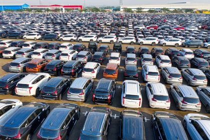Vista aérea de fileiras de automóveis novos estacionados em uma área industrial.